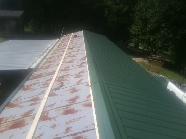 Old rusted panels beside newly installed green metal roofing — Wind Damage Roof Repair by Roofing Brothers in Tipton