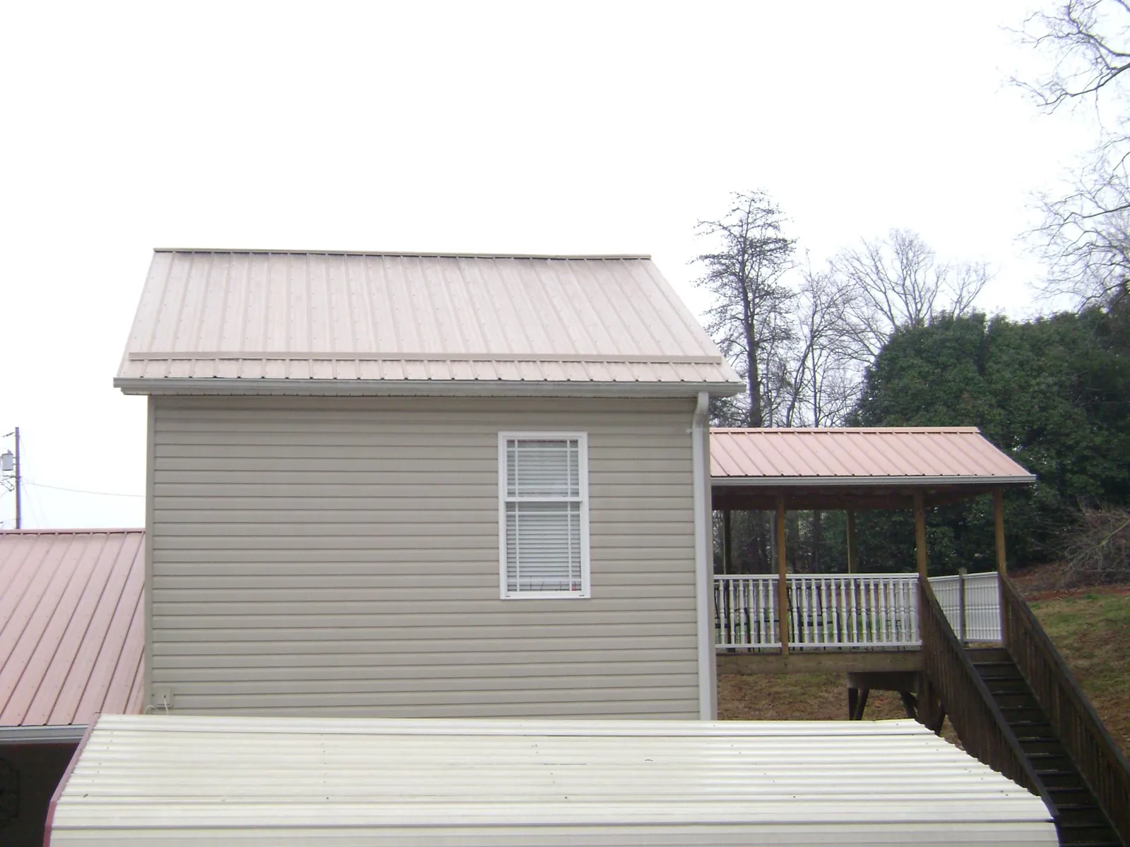 Tan metal roofs on a two story addition and attached porch, from a Roof Replacement job in Tipton